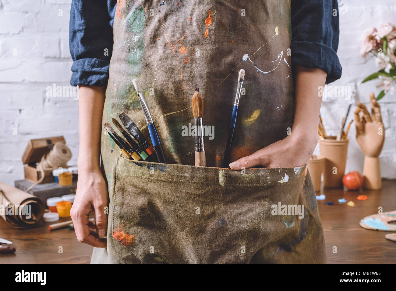 cropped image of artist with brushes and hand in apron pocket Stock
