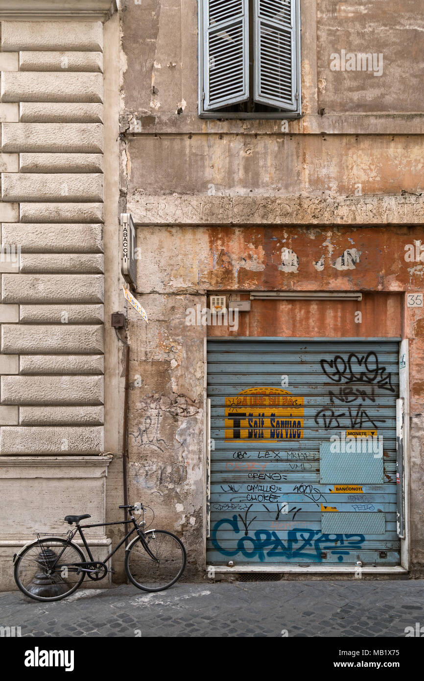 An old bike leaning against the wall of a graffiti covered shutter where a self service 'Tabacchi' (tobacconist) once was, a scene from the back stree Stock Photo
