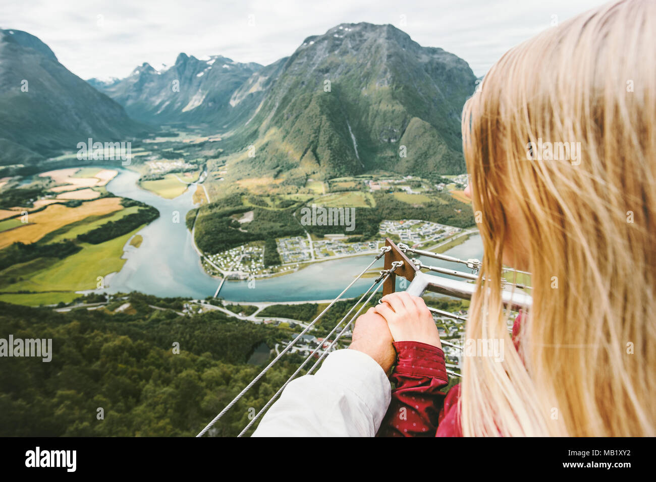 Couple Man and Woman holding hands enjoying mountains landscape Love and Travel Lifestyle adventure vacations in Norway Rampestreken viewpoint Stock Photo