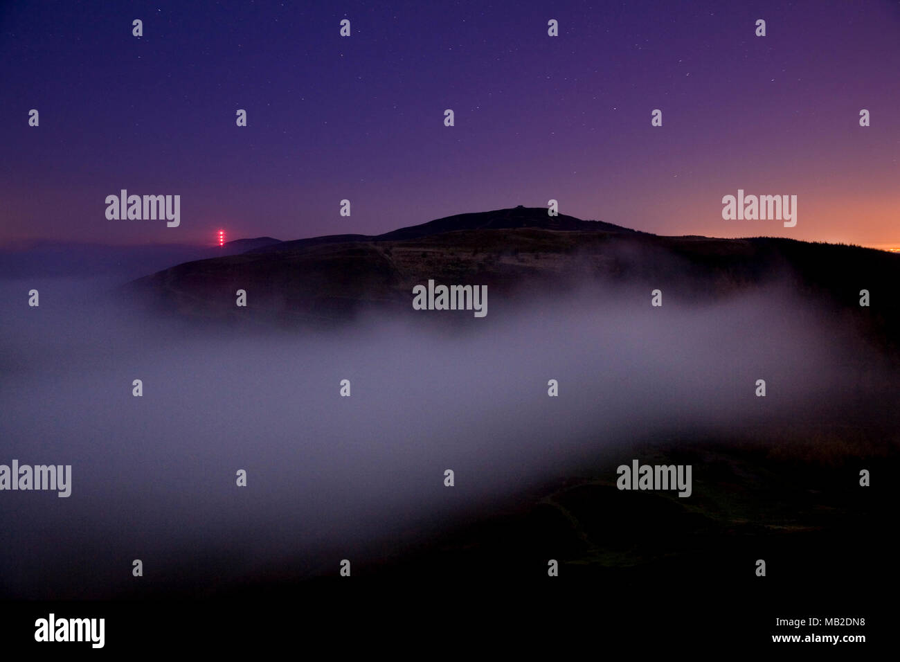 Moel Famau hill in North Wales shrouded in fog before dawn with stars above and the red lights of the Moel y Parc transmitter in the background Stock Photo