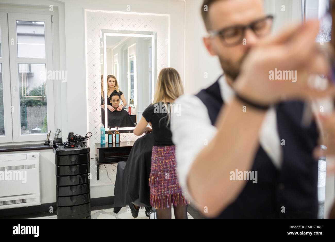 Portrait of mirror reflection of hairdresser preparing customer for