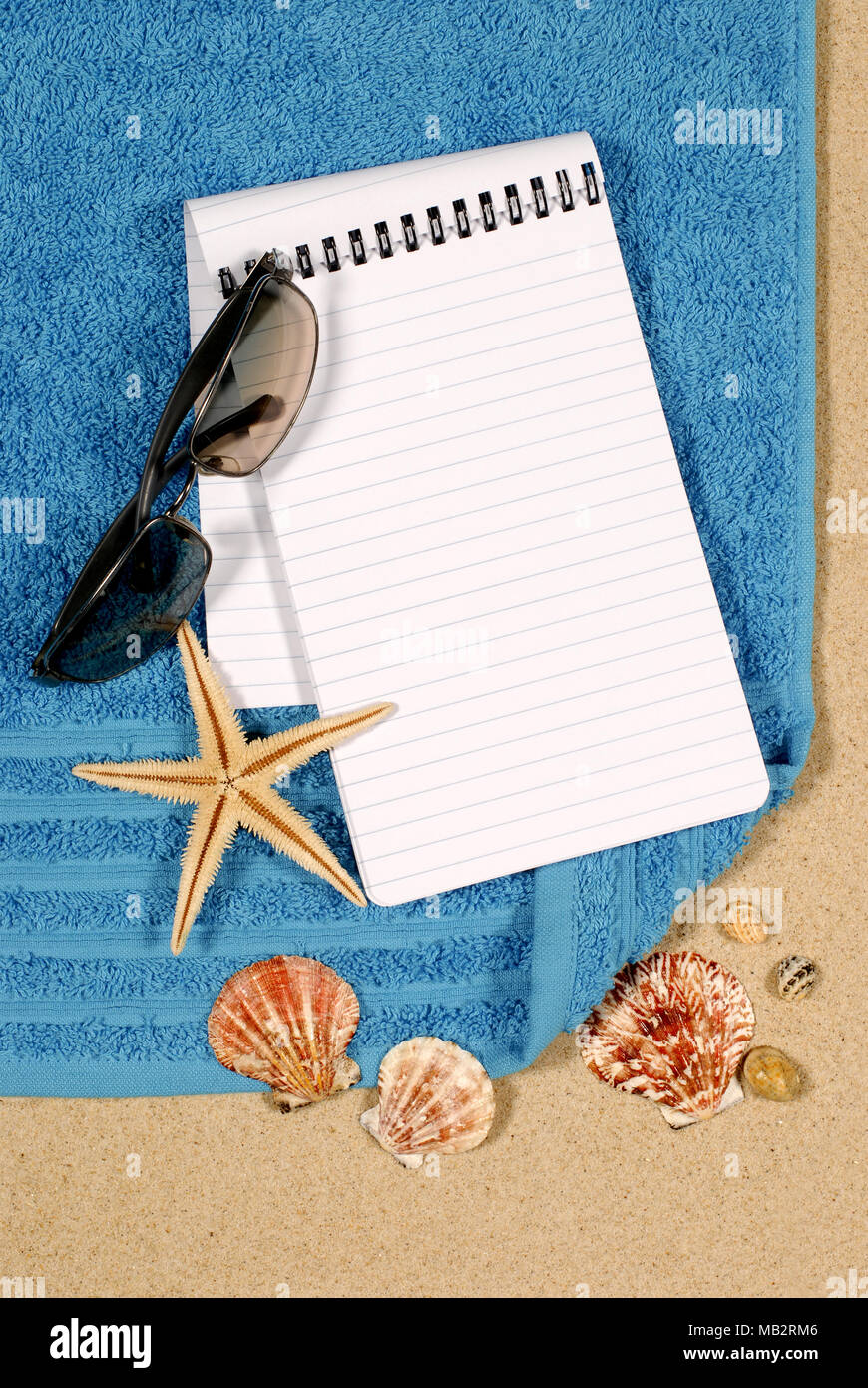 Beach scene with shells, starfish, towel, sunglasses and blank spiral notepad Stock Photo