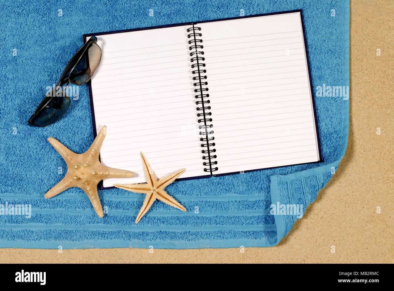 Beach scene with starfish, towel, sunglasses and blank writing book Stock Photo