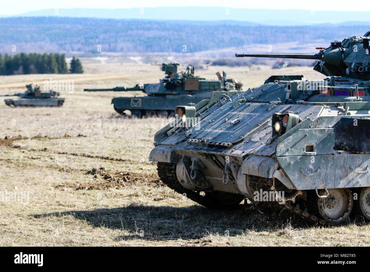 A M2 Bradley fighting vehicle and a group of M1 Abrams tanks with the 2nd Armored Brigade Combat Team, 1st Infantry Division, secure an area during a Robotic Complex Breach Concept demonstration at Grafenwoehr Training Area, Germany, April 6, 2018. The Robotic Complex Breach Concept employes the use of Robotic and Autonomous Systems (RAS) for intelligence, suppression, obscuration, and reduction missions. (U.S. Army photo by Spc. Hubert D. Delany III / 22nd Mobile Public Affairs Detachment)  Stock Photo