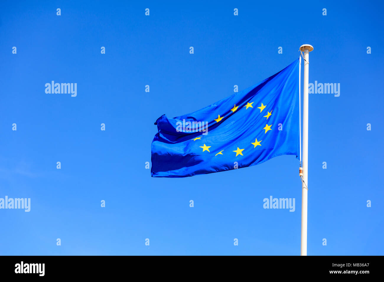 EU flag. European Union flag on a flagpole waving in the opposite direction on a blue sky background Stock Photo