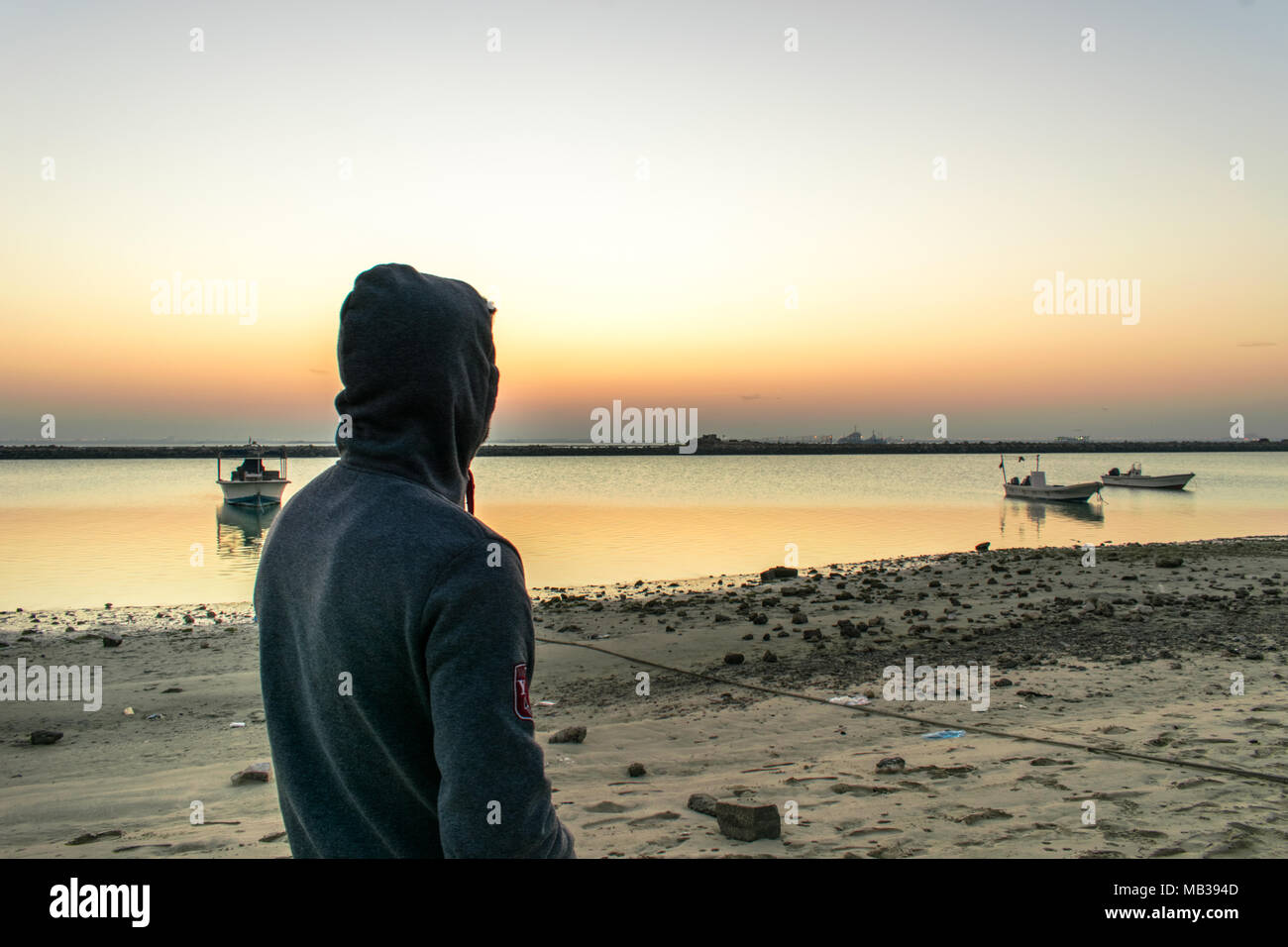 closeup of a man looking to the sunset at a beach and sea boats in the ...