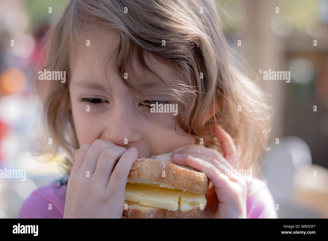 Young girl taking a bite out of a large cheese sandwich Stock Photo