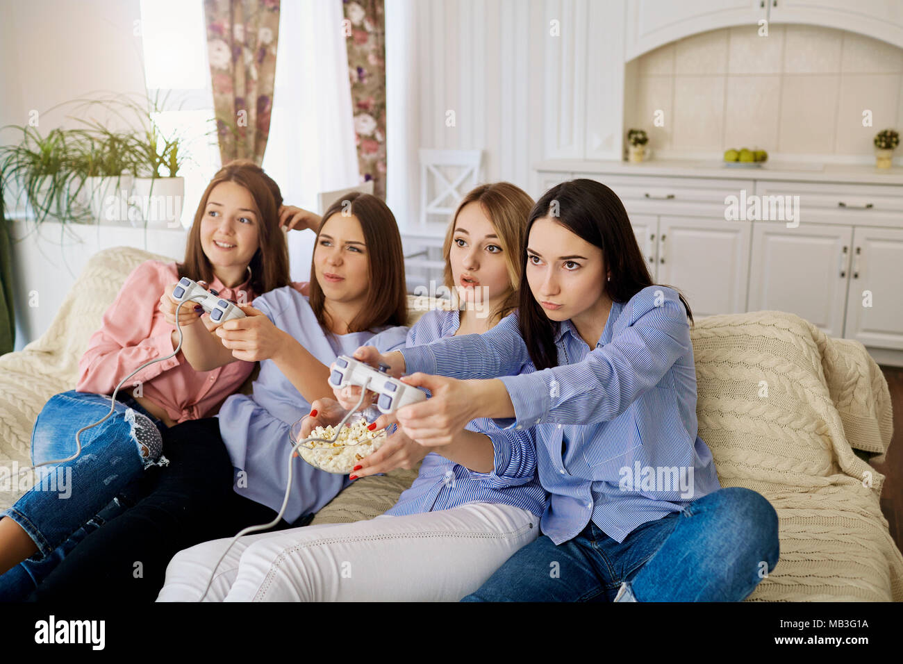 Girlfriends are playing video games sitting on the couch in the room. Stock Photo