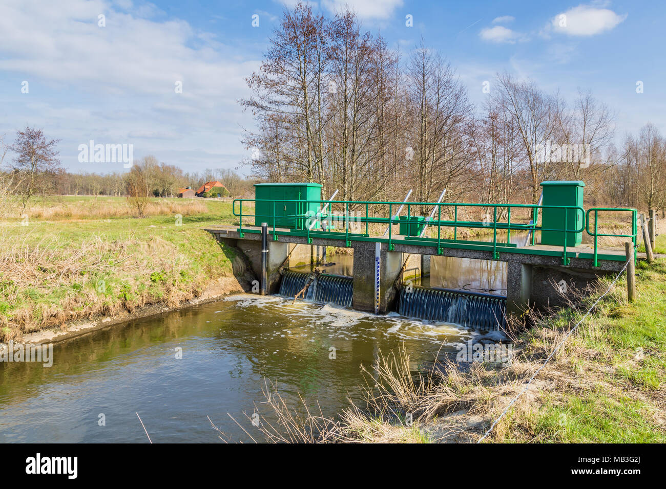 Narrow bridge over a small river in a nature reserve in the Netherlands. There is a weir under the bridge. It is at the end of the winter season. Stock Photo