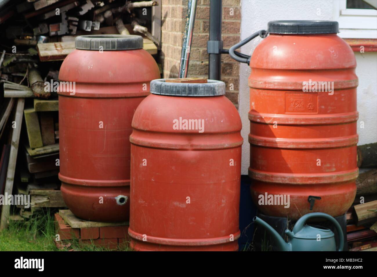 Three red water butts and green watering can in a garden Stock Photo