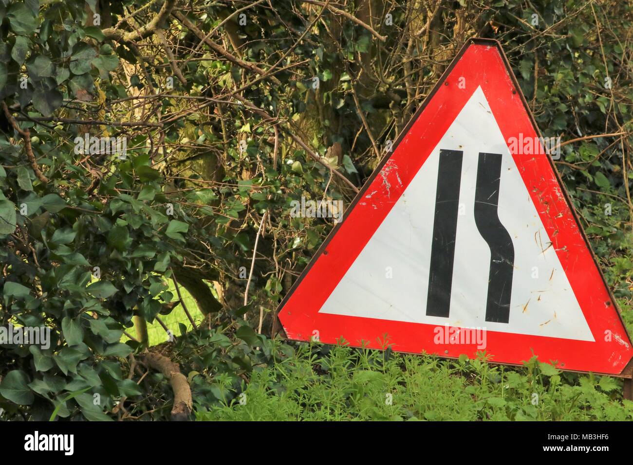 Red border triangle road sign at side of the road showing narrow right side of road for traffic Stock Photo