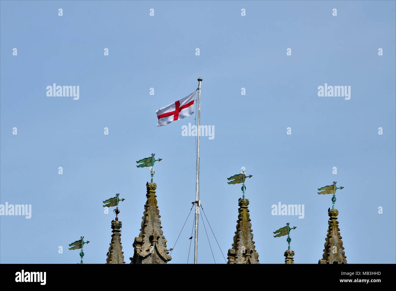 St George's flag flying in the wind on top of a church next to spirals / towers against a clear blue sky Stock Photo