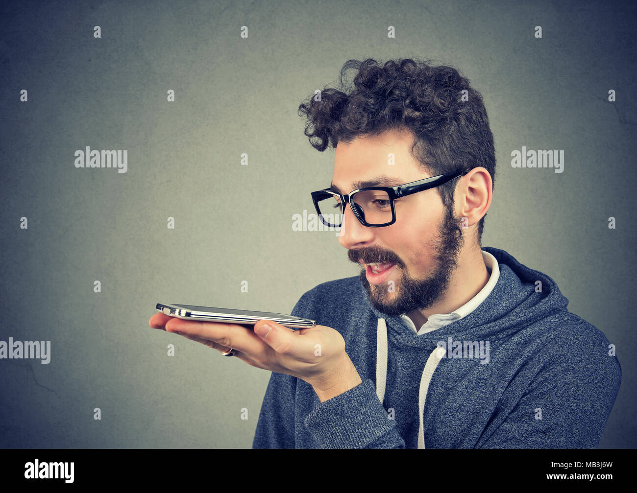 Hipster man in glasses using a smart phone voice recognition function isolated on wall background Stock Photo