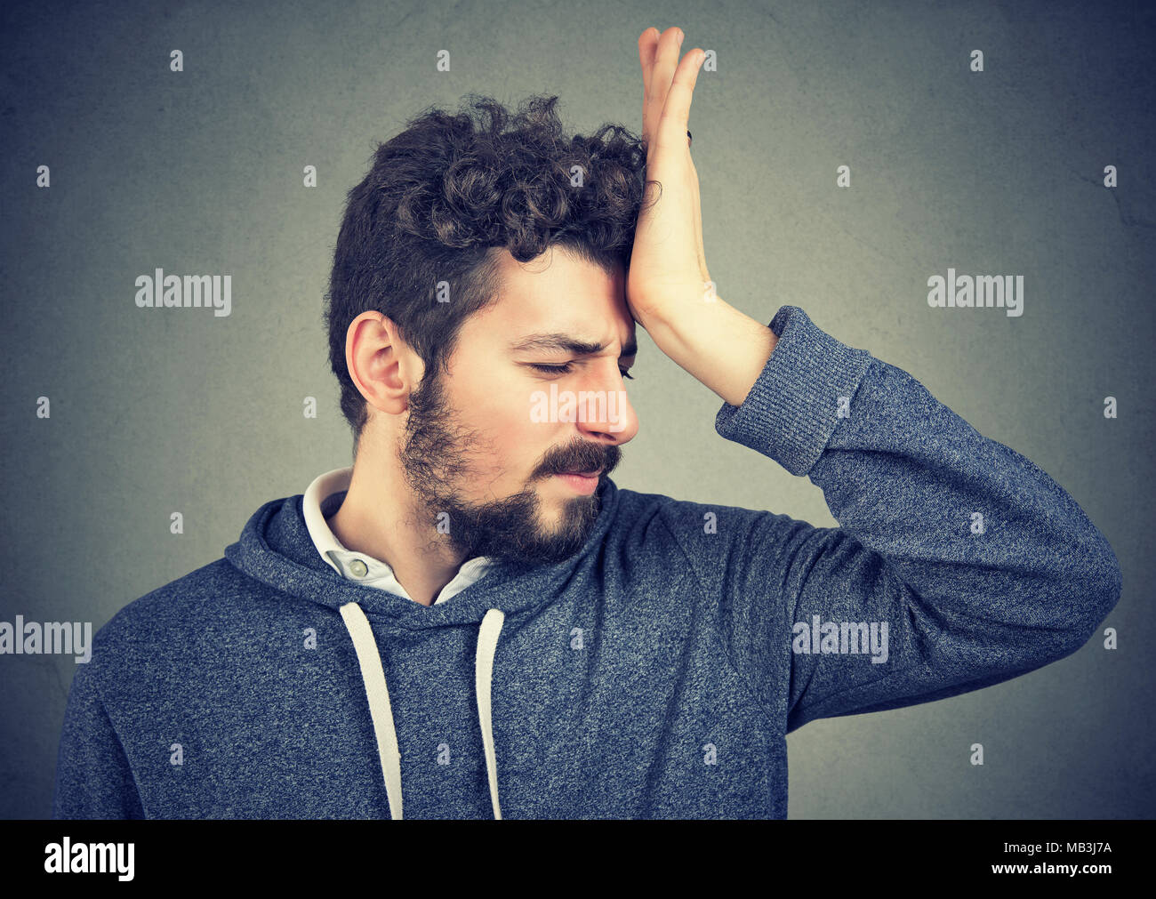 Regrets wrong doing. Portrait silly young man, slapping hand on head having a duh moment isolated on gray background. Negative emotion expression feel Stock Photo