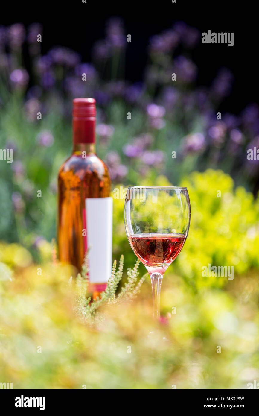 Rose wine in glass with bottle amongst flowers Stock Photo