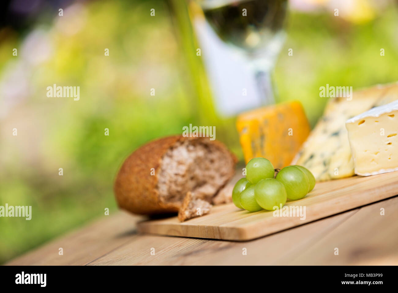 Selection of green grapes, cheese platter and white wine on wooden serving board on a sunny day Stock Photo