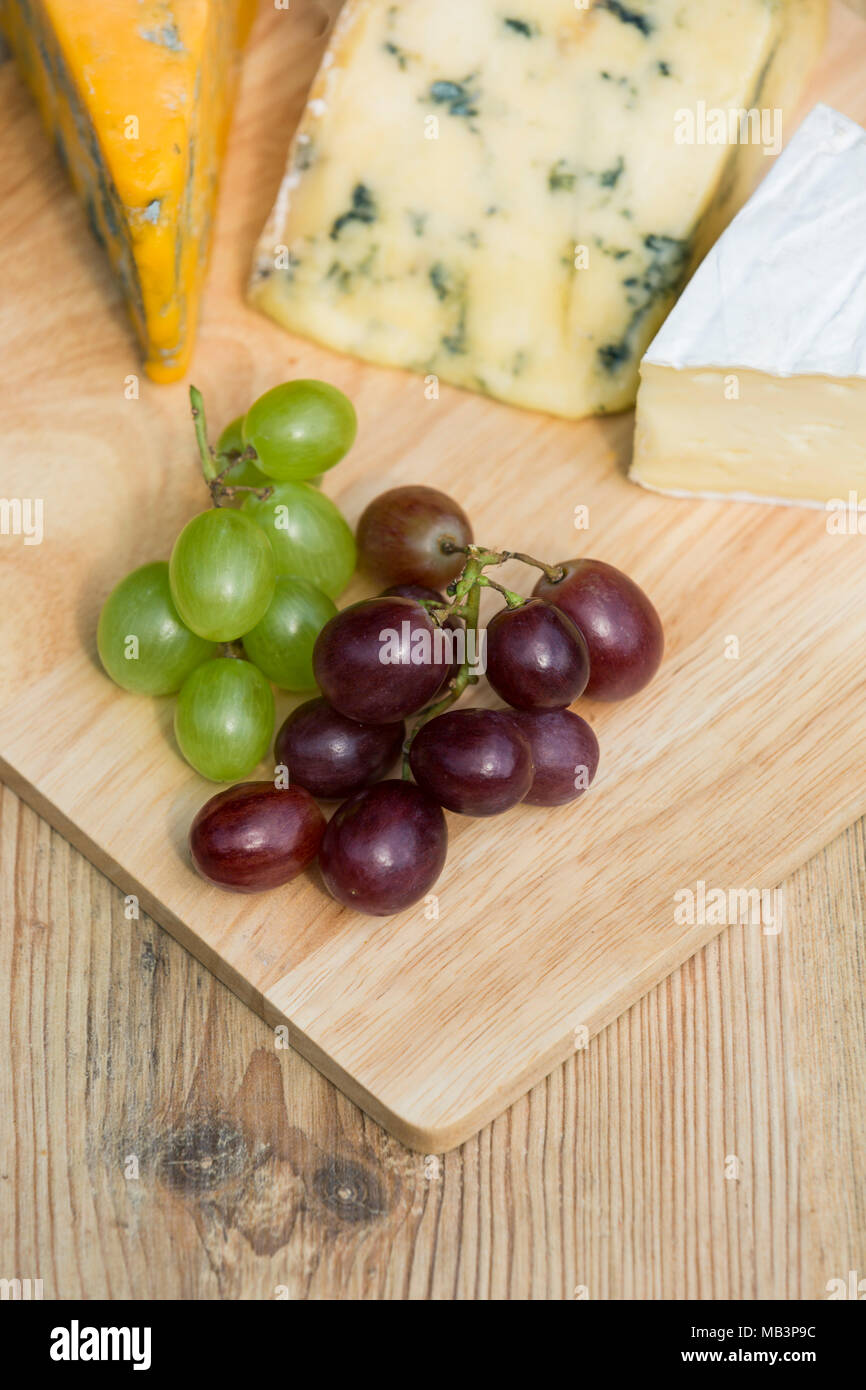 Overhead aerial view of a selection of red and green grapes with cheese platter on wooden serving board on a sunny day Stock Photo