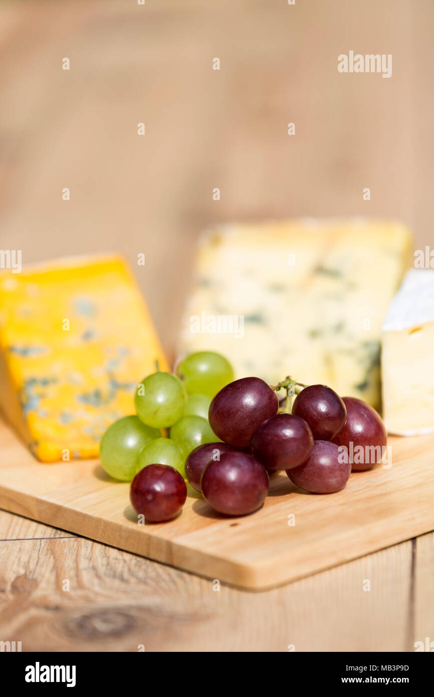 Selection of red and green grapes with cheese platter on wooden serving board on a sunny day Stock Photo