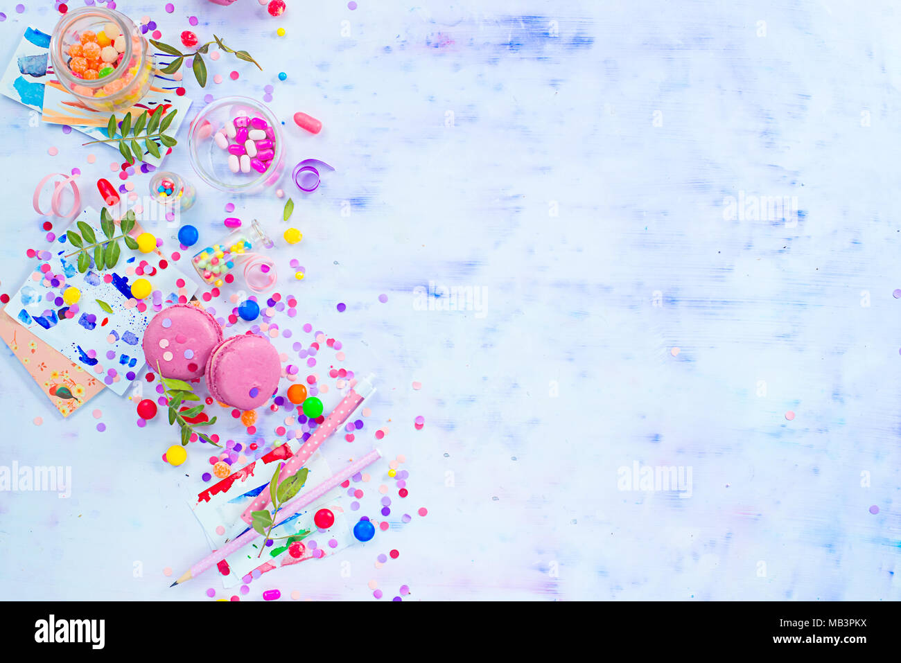 Colorful celebration flat lay with party supplies, confetti and sweets. Pink macarons overhead scene with copy space. Stock Photo