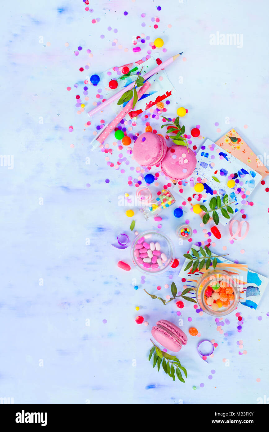 Colorful celebration flat lay with party supplies, confetti and sweets. Pink macarons overhead scene with copy space. Stock Photo