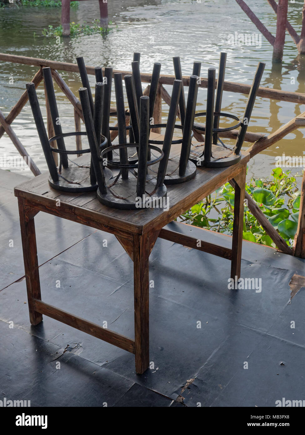 Restaurant on raft by canal in countryside was closed with black wooden and metal chairs put on brown wooden tables Stock Photo