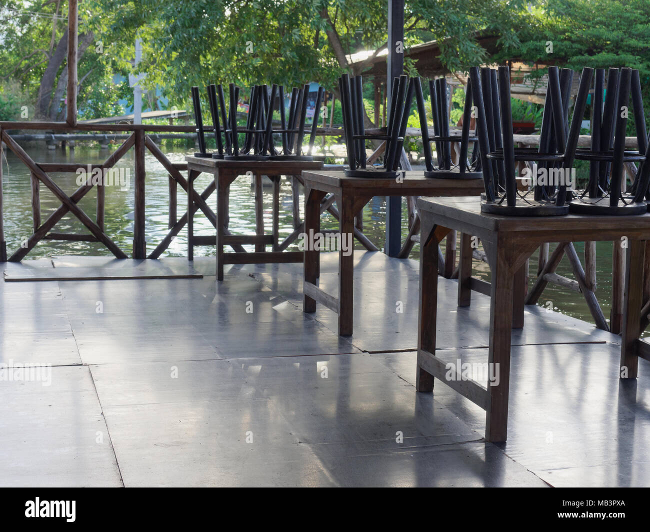 Restaurant on raft by canal in countryside was closed with black wooden and metal chairs put on brown wooden tables Stock Photo