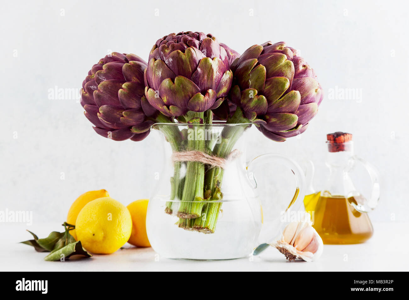 Fresh bunch of purple artichokes in a decanter with water on white background with lemon, olive