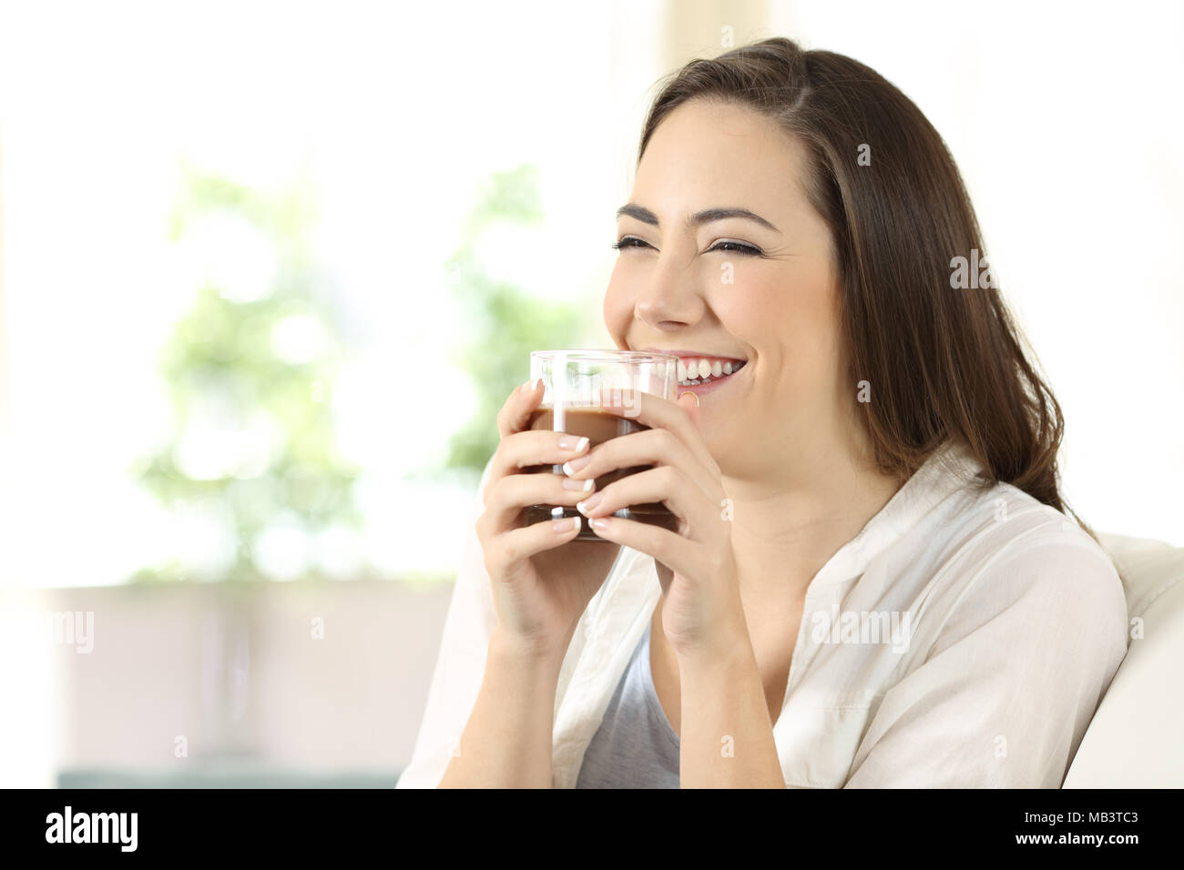 Candid girl drinking cocoa shake sitting on a couch in the living room at home Stock Photo