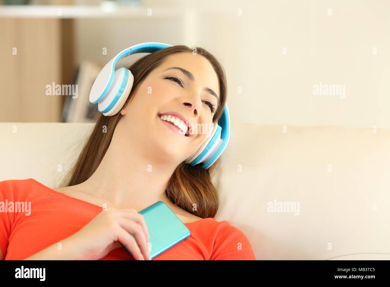 Candid girl wearing headphones listening to music sitting on a couch in the living room at home Stock Photo