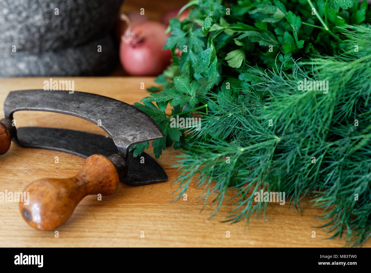https://c8.alamy.com/comp/MB3TW0/rustic-double-blade-mezzaluna-herb-cutter-on-wood-board-next-to-a-large-bunch-of-fresh-herbs-MB3TW0.jpg
