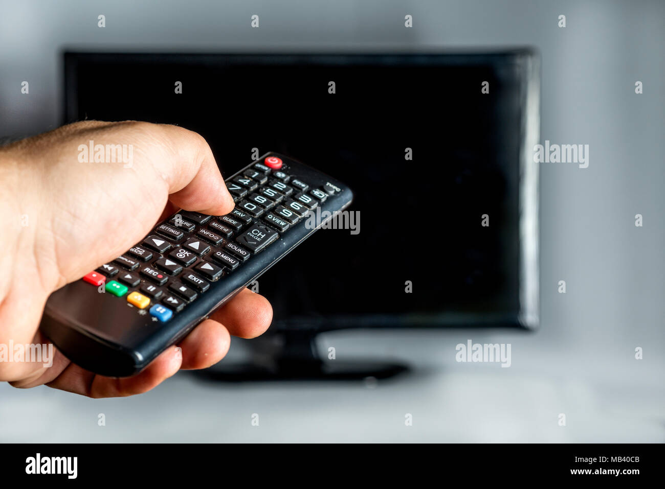 hand holding a remote control and behind a tv on white background Stock Photo