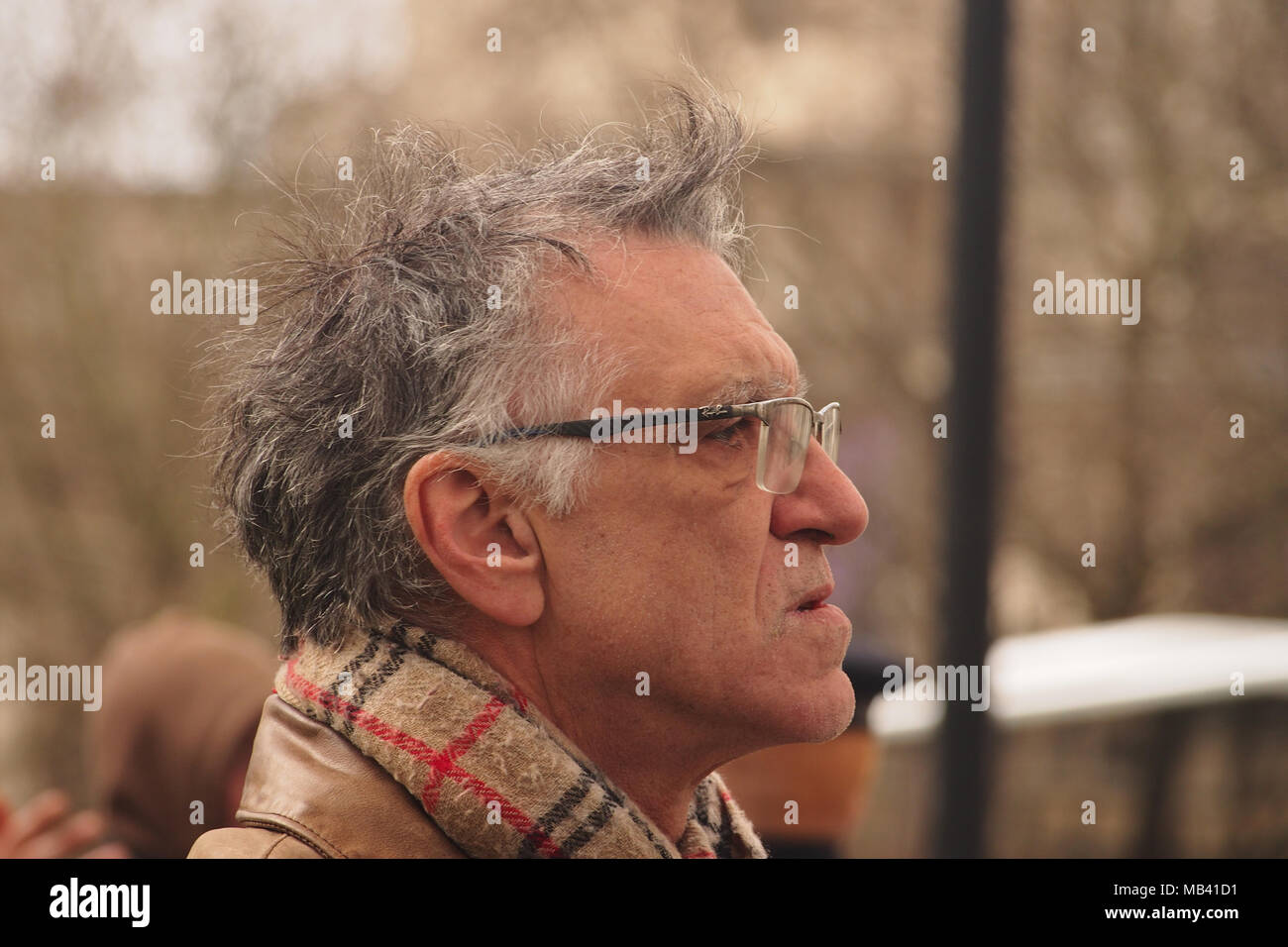An older man standing in London on a cold day wrapped up in a scarf watching the world go by Stock Photo