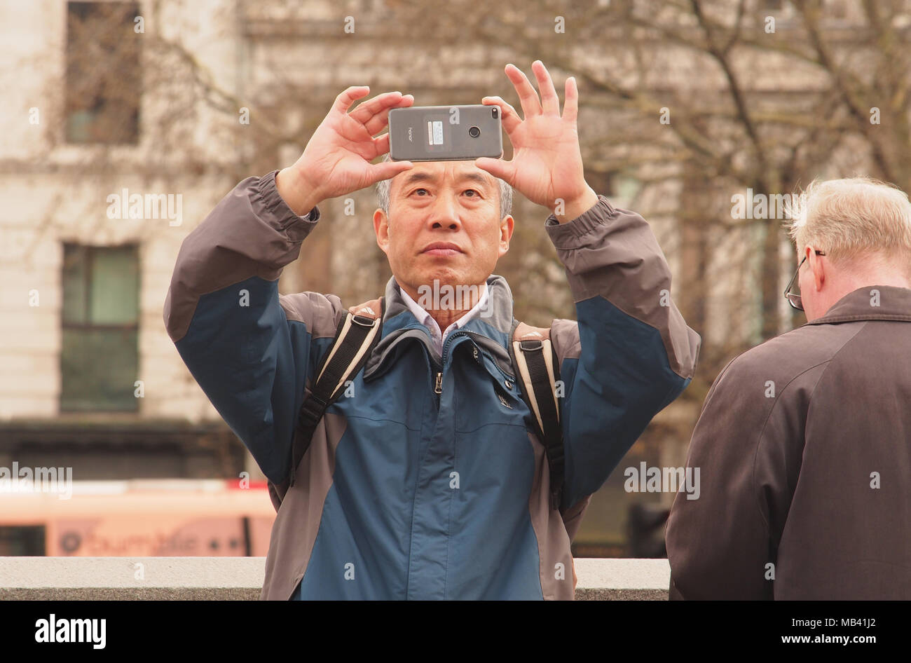 A man holding a smartphone above his eye level composing a photograph in Trafalgar Square, London Stock Photo
