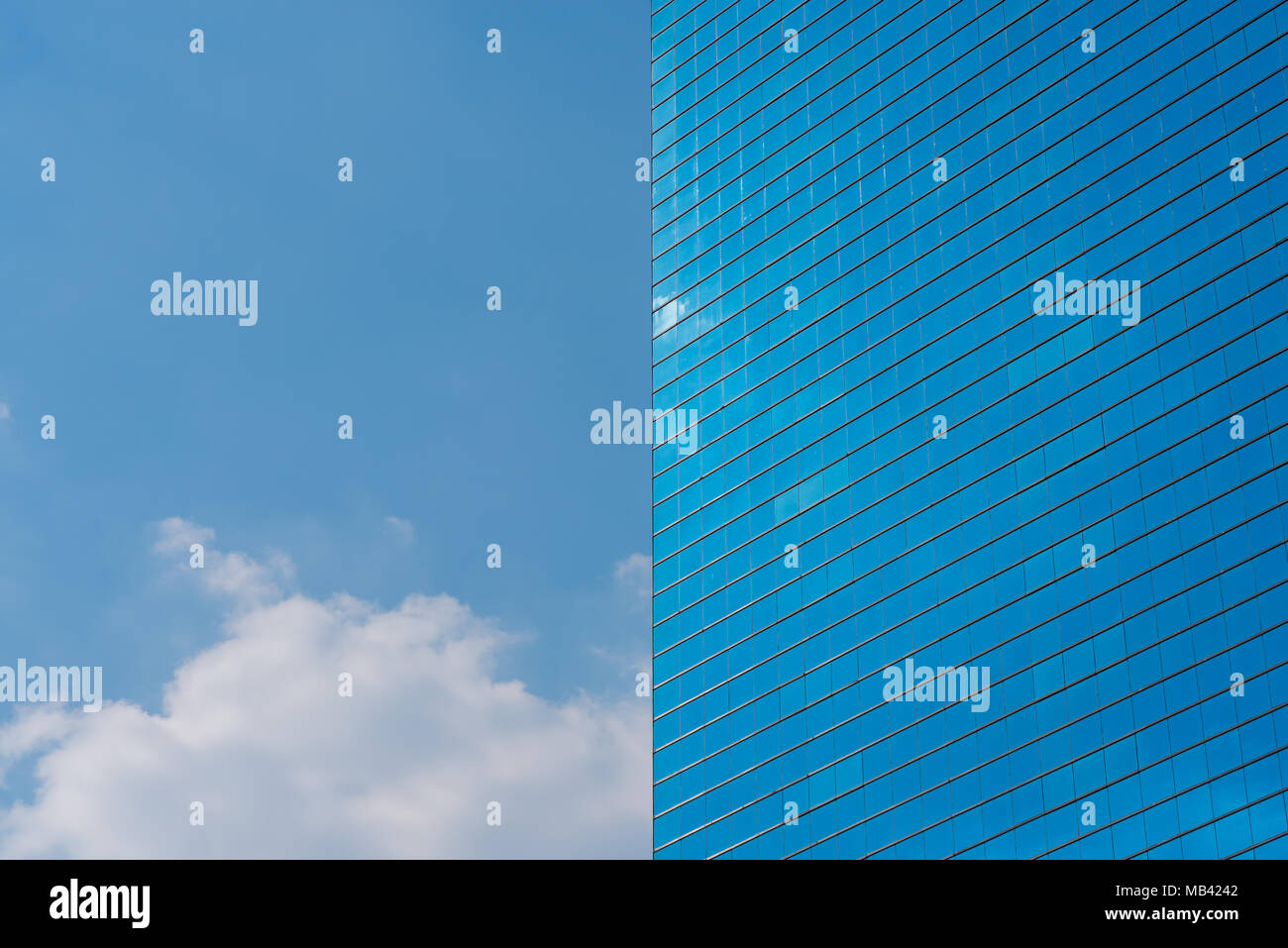 Blue office glass building and blue sky with a cloud - horizontal photo. Skyscraper and the sky divide the frame into two symmetrical halves Stock Photo