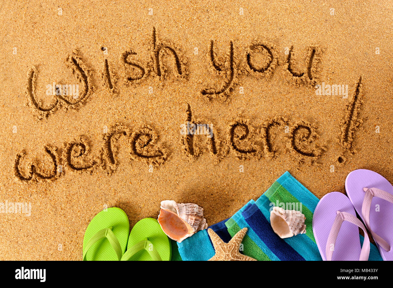 Classic postcard message written on a sandy beach, with beach towel ...