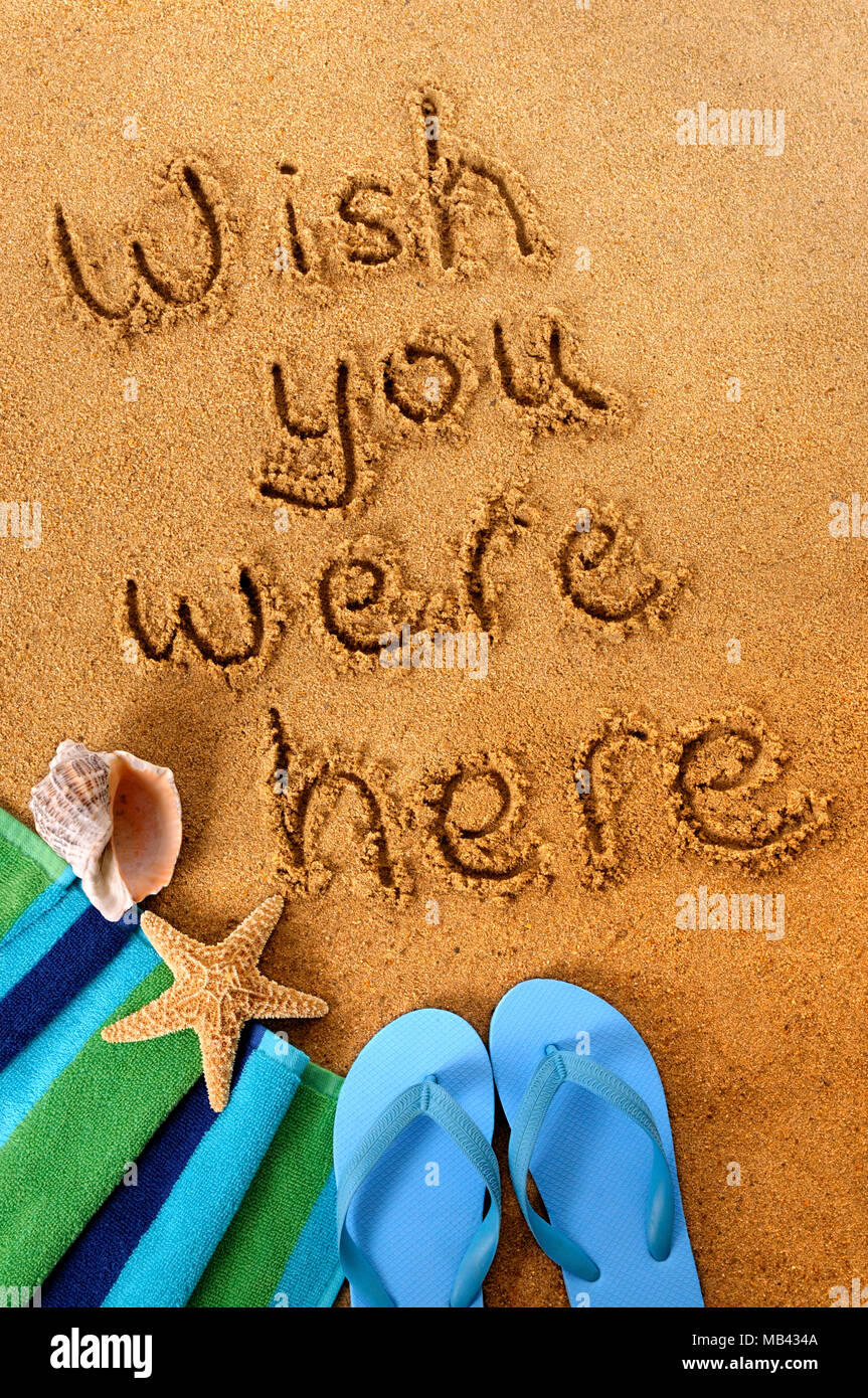 Classic postcard message written on a sandy beach, with beach towel ...