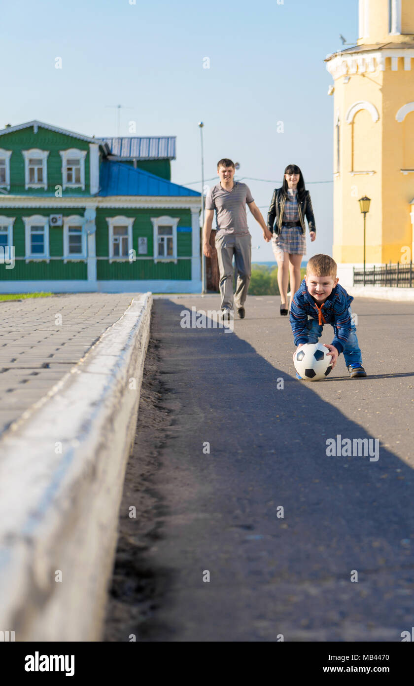 Cute little boy is walking in a park with his parents and carrying soccer ball Stock Photo