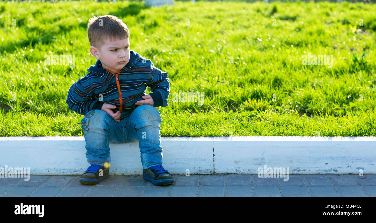 Serious capricious boy is sitting on the road Stock Photo