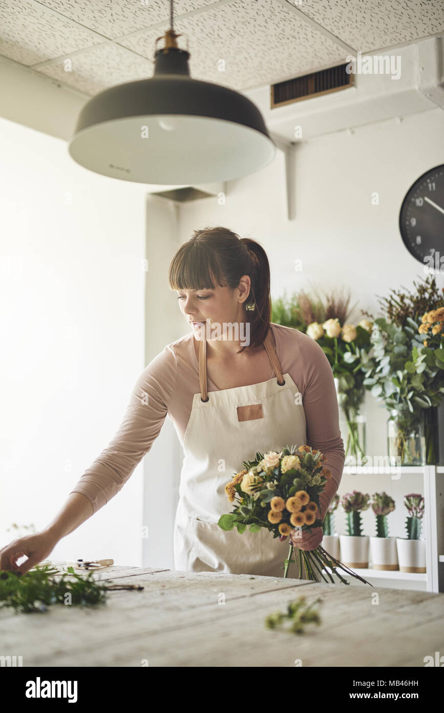 Young female florist working at a table in her flower workshop arranging a bouquet of roses and mixed flowers Stock Photo