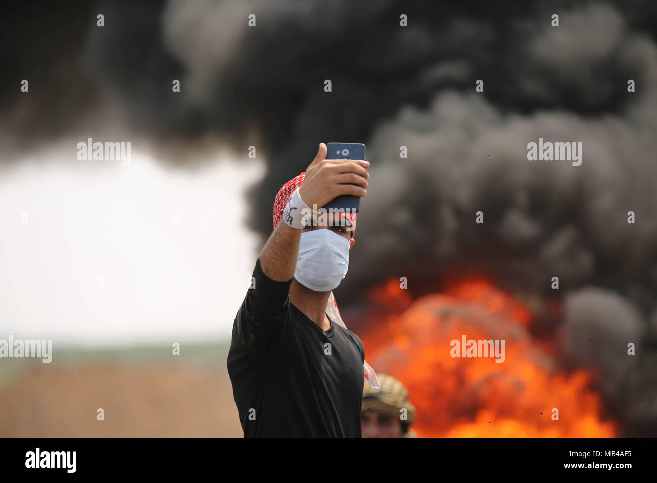 Gaza City, Gaza Strip, Palestinian Territory. 5th Apr, 2018. A Palestinian protester takes a selfie as others burn tyres to protect themselves from shots of Israeli soldiers during clashes at the Israel-Gaza border in a tent city protest demanding the right to return to their homeland, in east of Gaza city on April 6, 2018 Credit: Dawoud Abo Alkas/APA Images/ZUMA Wire/Alamy Live News Stock Photo