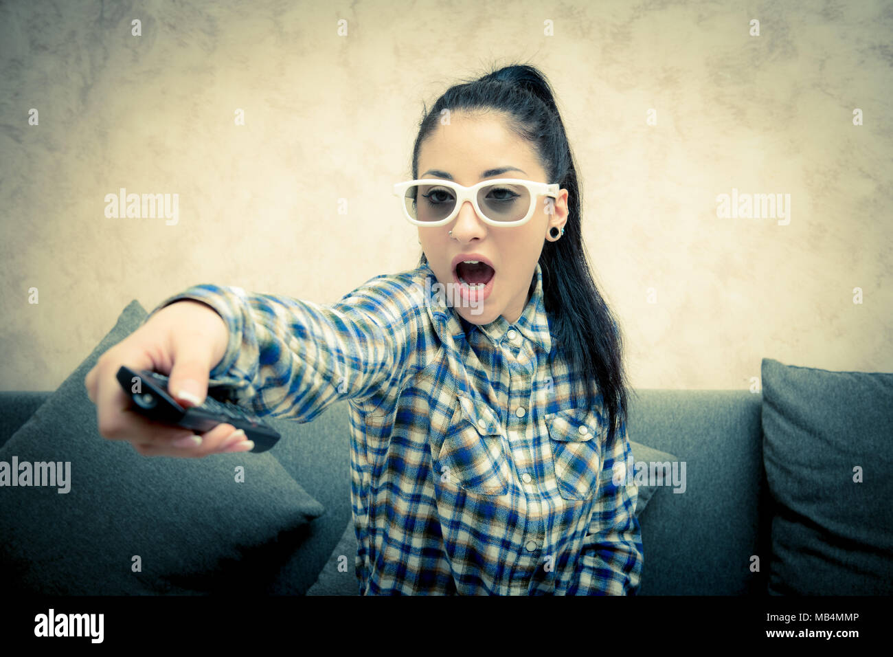 Teen girl with 3d eyeglasses at home amazed face expression with television remote control in hand Stock Photo