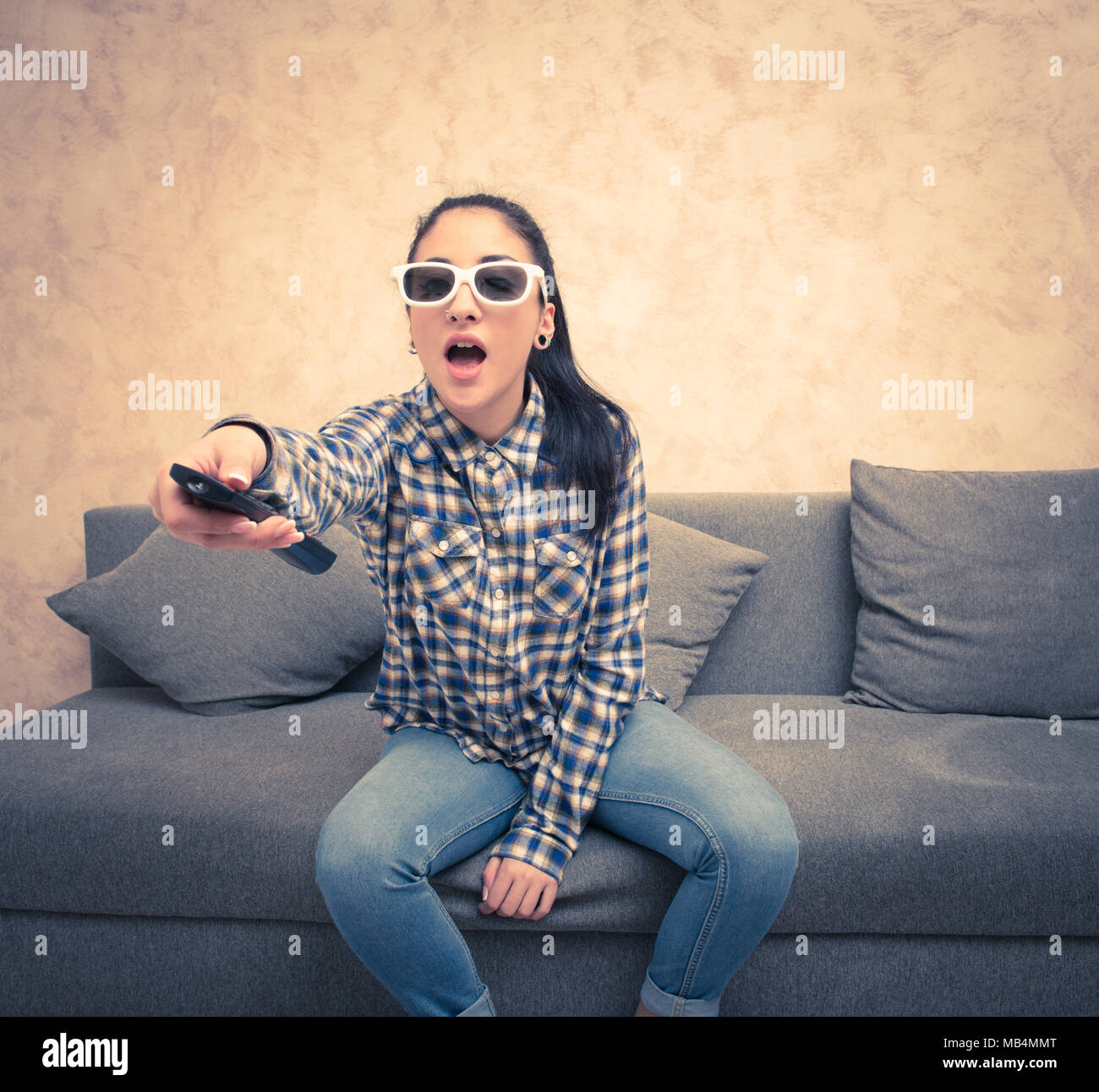 Teen girl with 3d eyeglasses at home amazed face expression with television remote control in hand Stock Photo