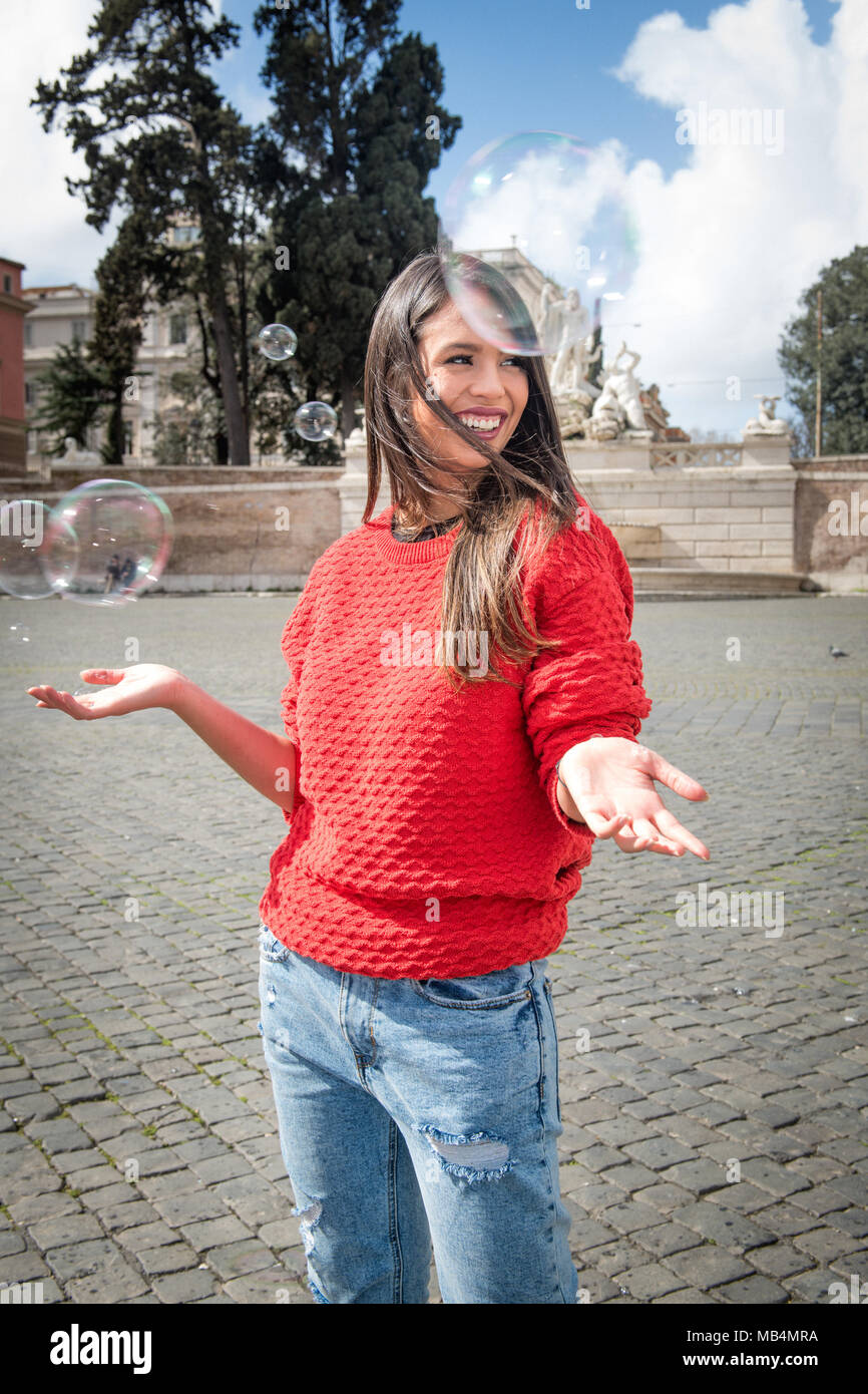 One young woman open arms looking out with soap bubbles around, outdoors Stock Photo