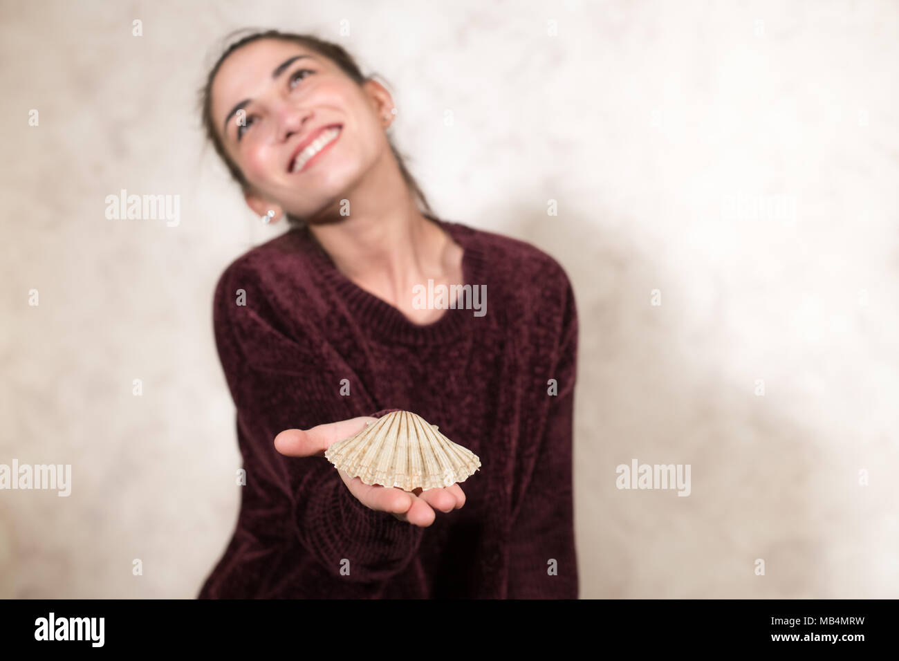 Human hands with sea shell offering and giving, woman smiling out of focus looking out, sea house concept Stock Photo