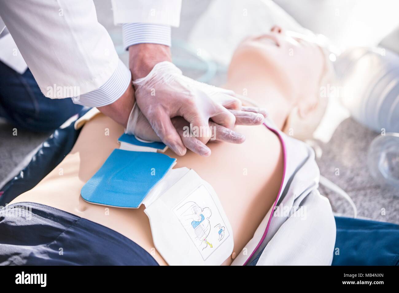 Doctor undertaking CPR training on dummies. Automated external defibrillator pads have been placed on the dummy's chest. Stock Photo