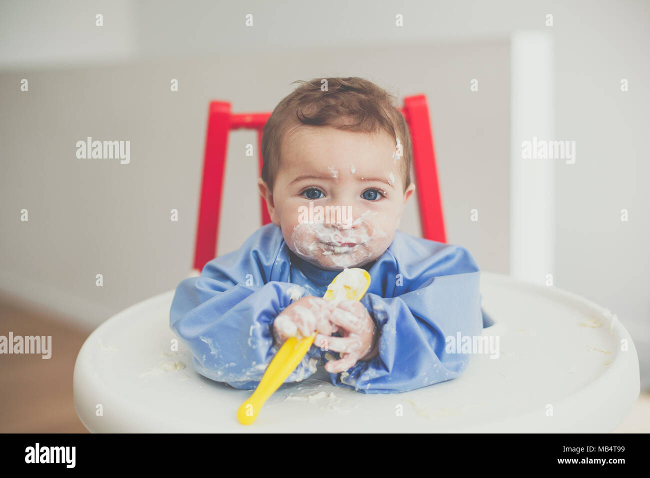6 month old baby boy feeding himself yoghurt with a spoon Stock Photo