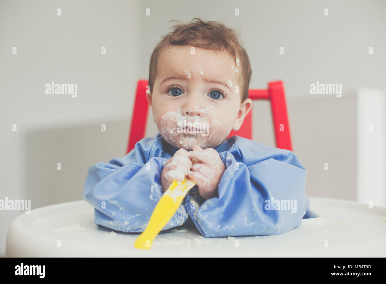 6 month old baby boy feeding himself yoghurt with a spoon Stock Photo