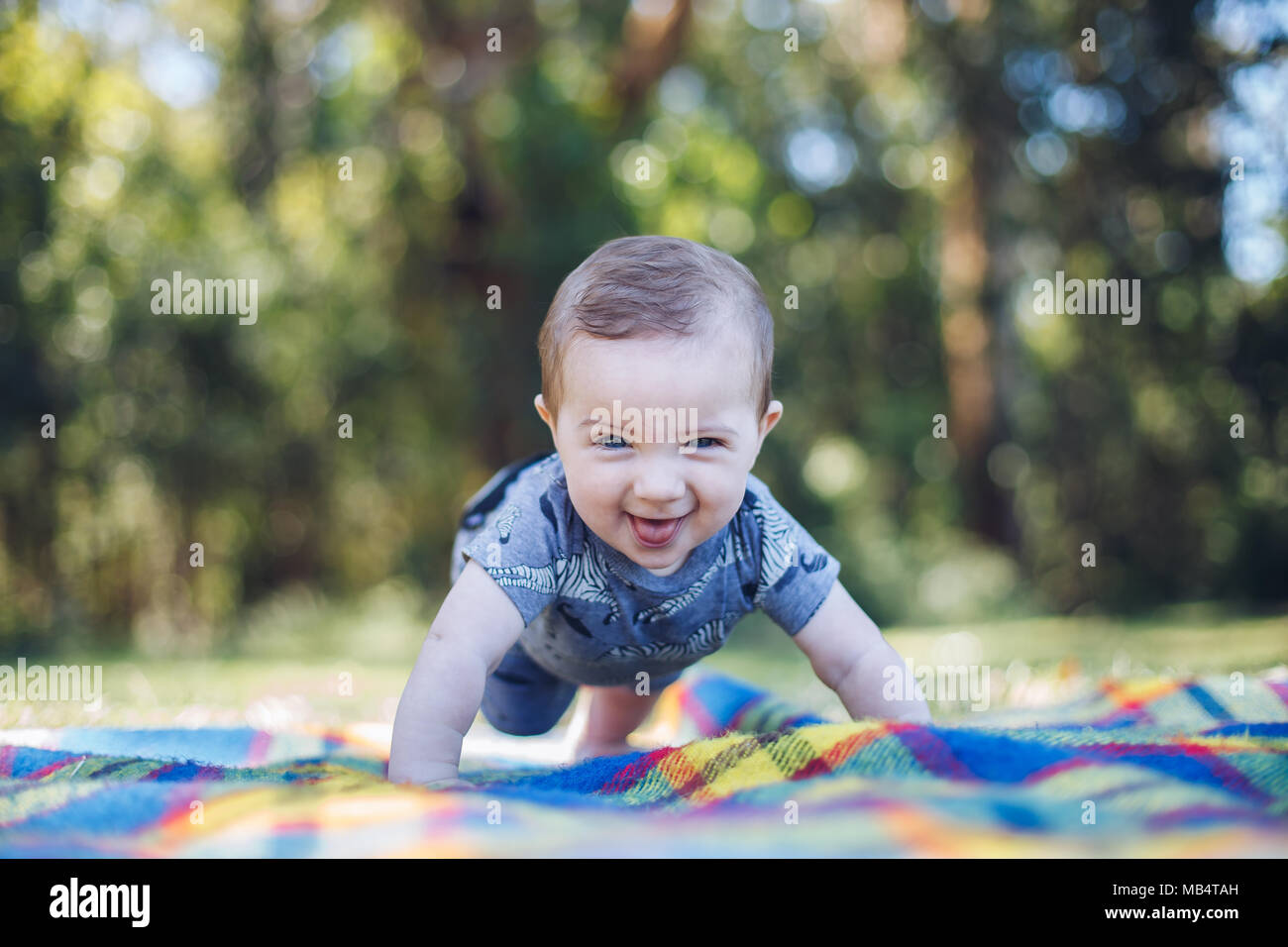 Happy 6 month old baby boy on his tummy on a picnic rug Stock Photo