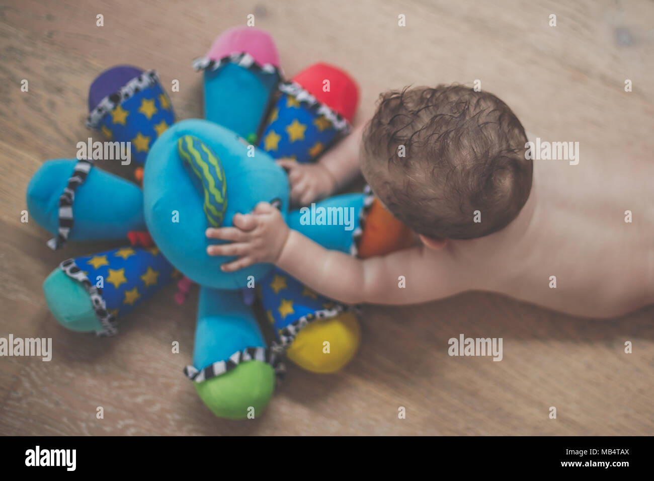 6 month old baby boy playing on the floor with a brightly colored toy Stock Photo