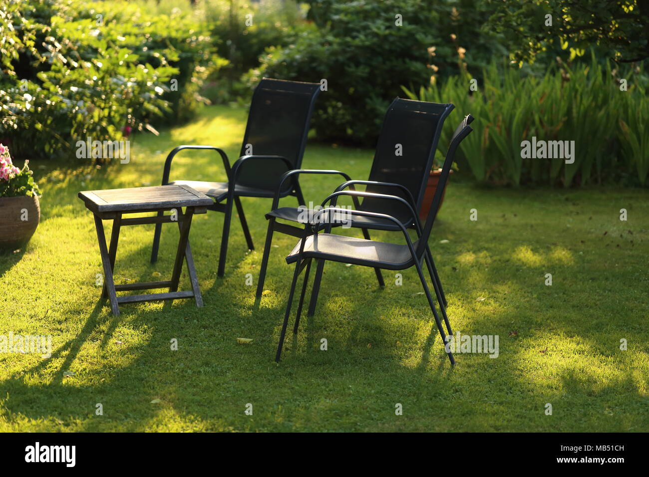 Chairs and table in the garden with greenery around Stock Photo - Alamy